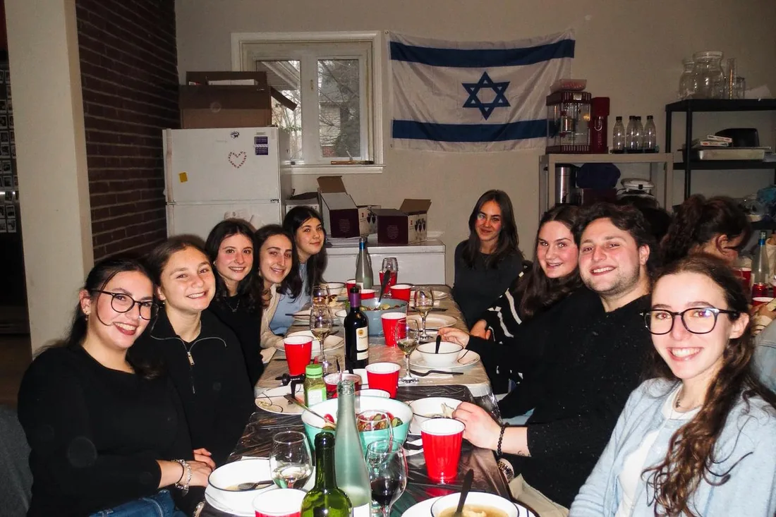 Students gathered around a Shabbat table beneath an Israeli flag