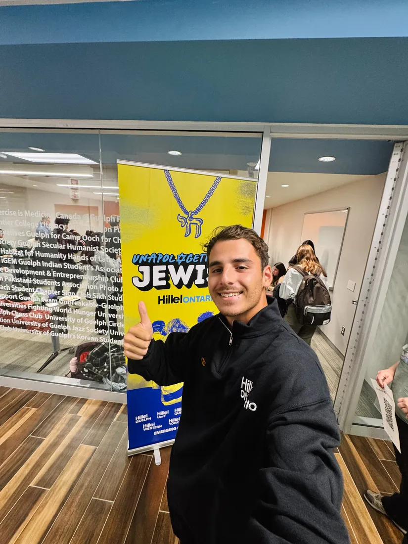 Yoel Levy gives a thumbs-up beside an Unapologetically Jewish banner on campus