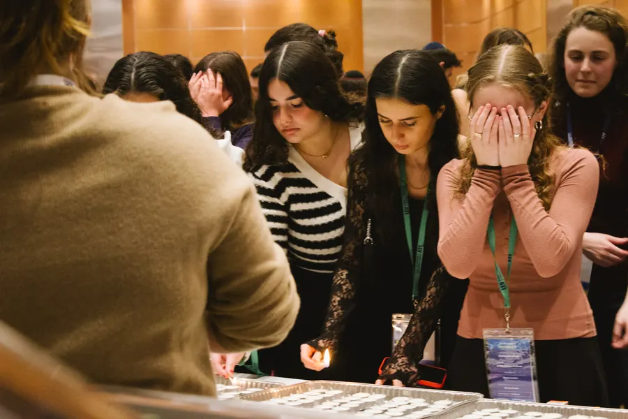 Students cover their eyes for the blessing over the Shabbat candles
