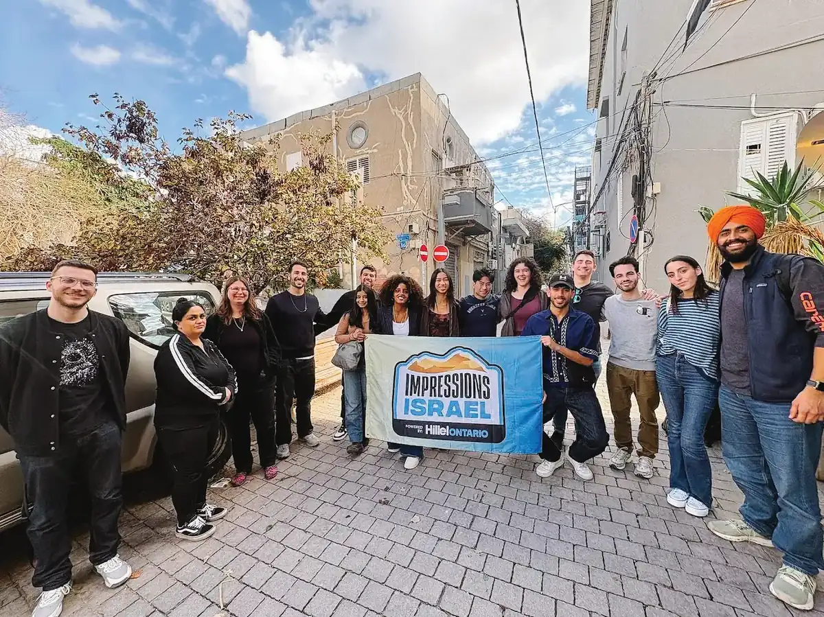 The Impressions cohort holds the program banner on a street in Israel